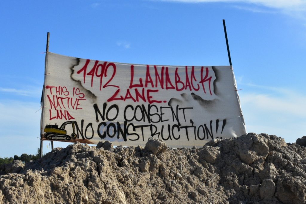 Elevated banner that reads: 1492 Landback lane. No consent, no construction. This is native land.